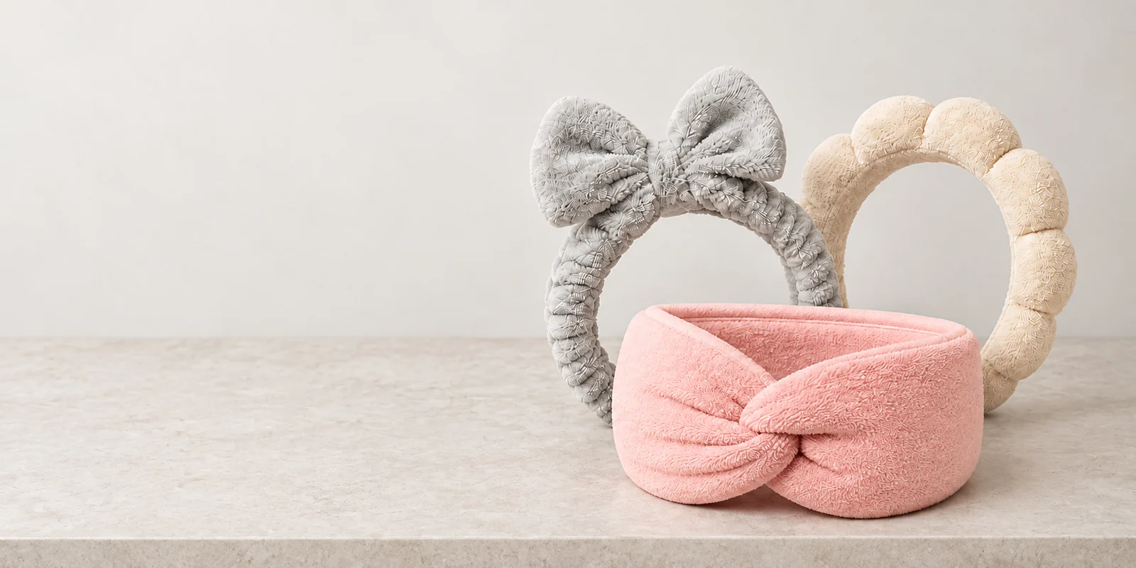 Three original makeup headbands on a neutral stone vanity counter
