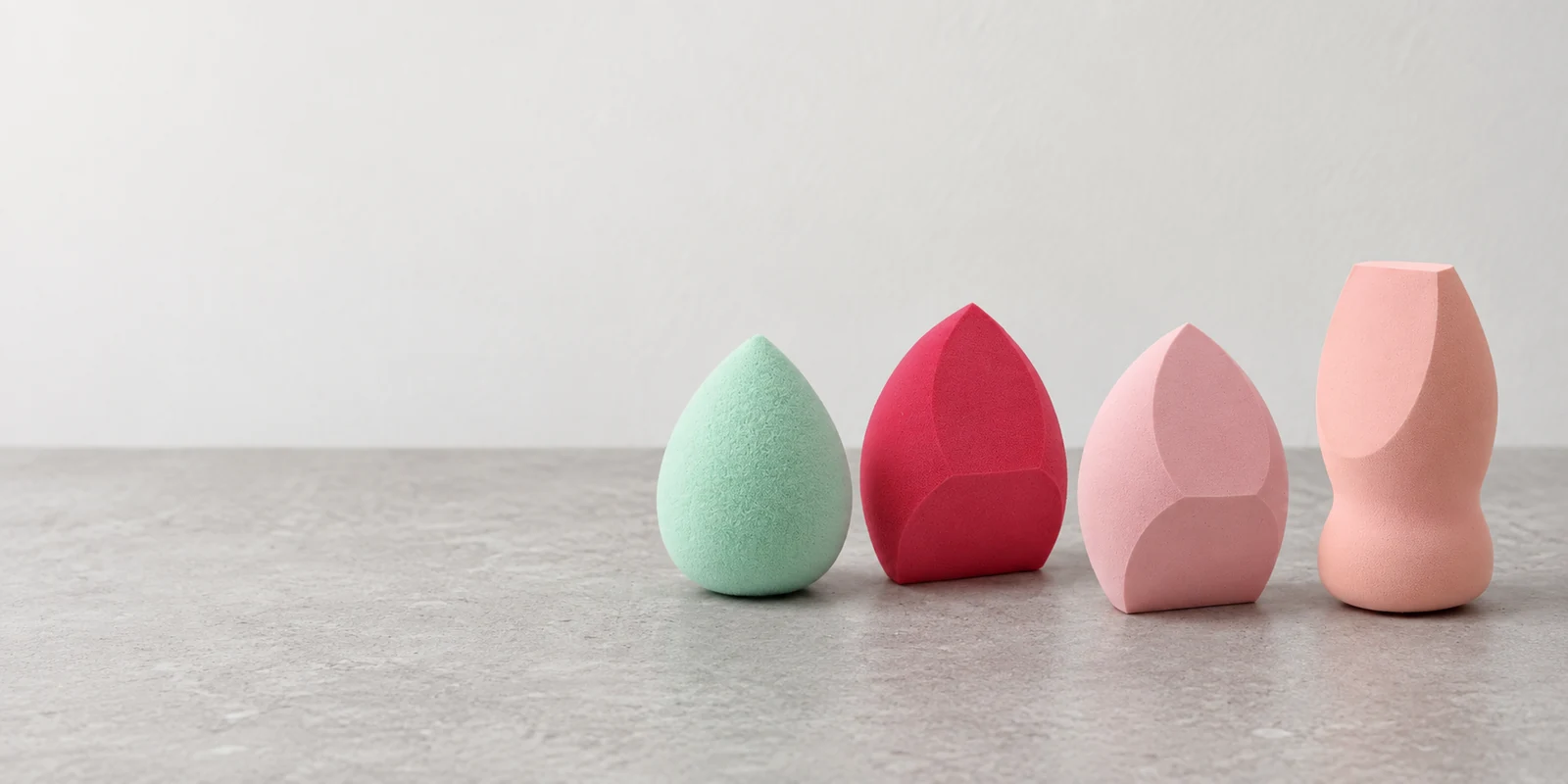 Four client-supplied makeup sponge shapes on a neutral stone vanity counter